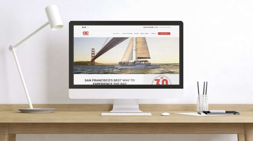 image of desktop computer on a minimal wooden desk showing the homepage design of the Adventure Cat Sailing website