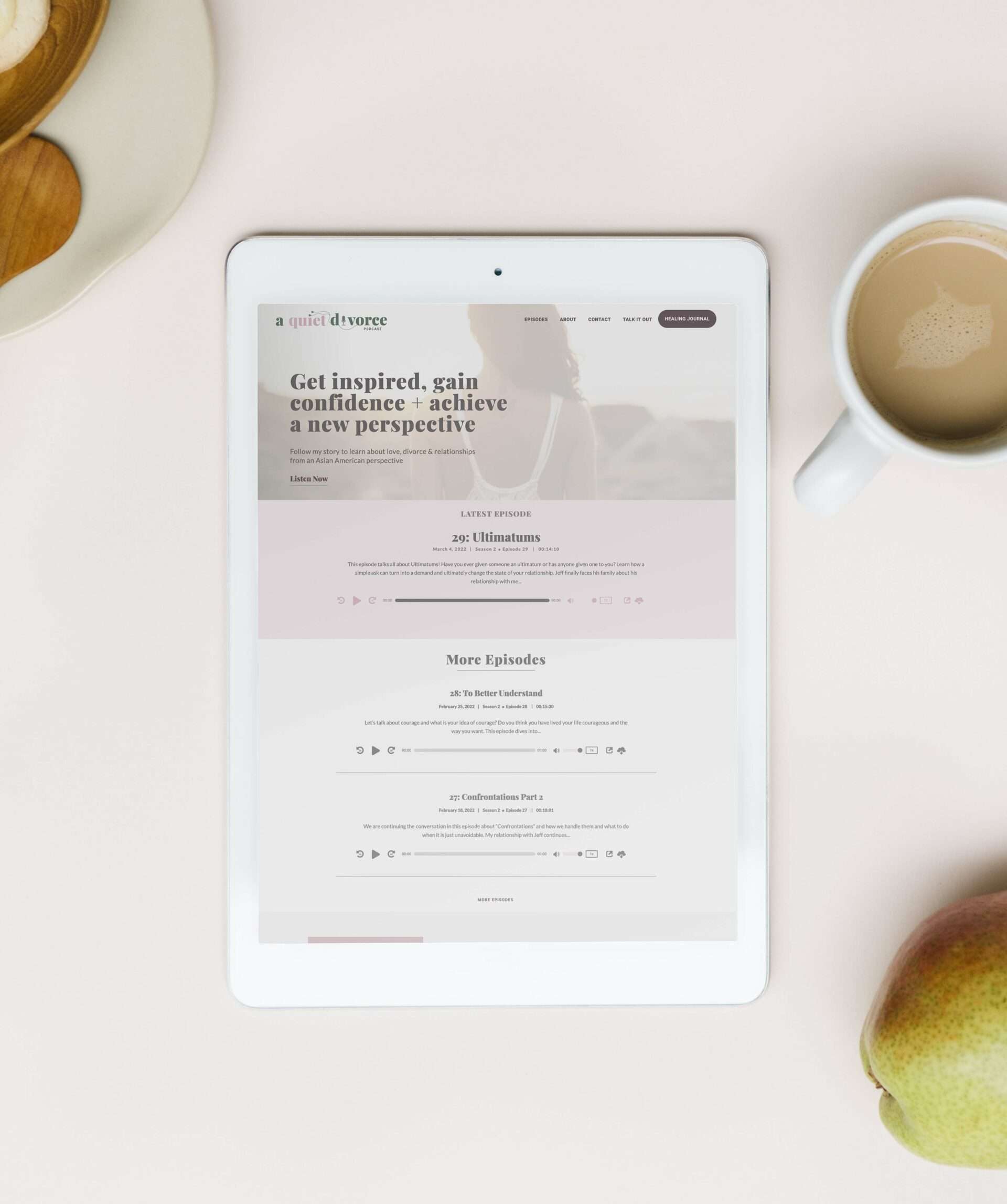 A Quiet Divorce podcast website shown on a white ipad against a pink table, a cup of coffee and some breakfast foods are nearby